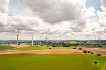 Obraz premium Drone view of modern wind farm on large agricultural landscape. Wind turbines spread across green and brown fields with moody clouds above, highlighting renewable energy in rural setting