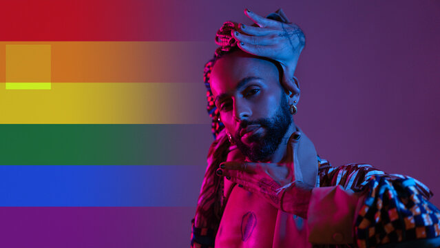 Neon light studio close-up portrait handsome black gay man looking camera. Seductive sexy man, transgender person dance in ultraviolet light on rainbow LGBT flag. Nightclub dancer nightlife concept