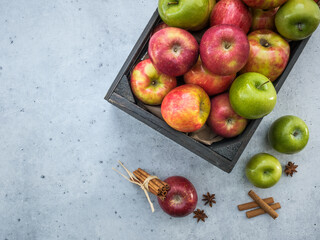 Overhead of black fruit harvest crate box with fresh red and green apples on a neutral light gray counter background. Fall autumn backdrop scene. Text copy space.