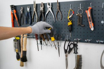 In a workshop setting, a person in gloves carefully selects a tool from a neatly organized...
