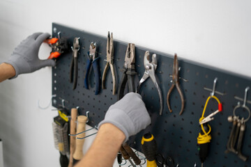 In a workshop setting, a person in gloves carefully selects a tool from a neatly organized pegboard, highlighting focus and preparation for a task ahead.