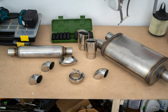 Exhaust system parts are arranged on a workbench, displaying various components for service, including mufflers and exhaust tips
