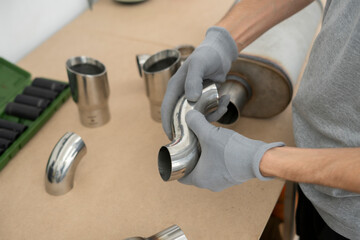 Worker fits together stainless steel elbow pipe joints using gloves in a well-organized workshop....
