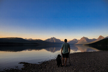 silhouette of a man and dog standing on a mountain lake