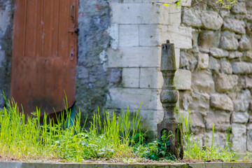 Old stone pedestal in overgrown courtyard with rustic brick wall and wooden door