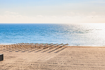 Empty sandy beach with straw umbrellas under clear sky and tranquil ocean view