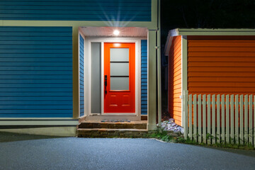A bright red metal door with three frosted glass windows. The wooden house is royal blue color with white trim. The wall is made of weatherboard or lap siding.