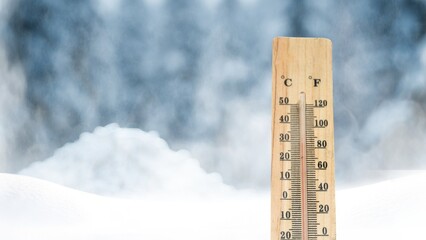 A thermometer on a background of snow-covered trees shows a low temperature in Celsius or...