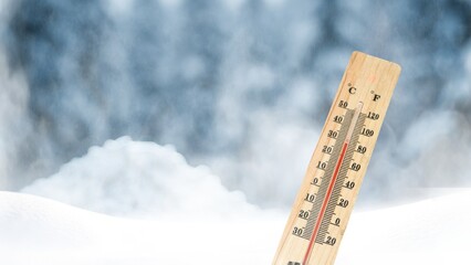 A thermometer on a background of snow-covered trees shows a low temperature in Celsius or...