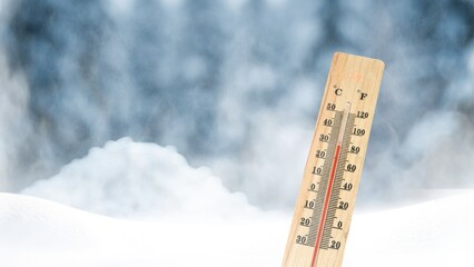 A thermometer on a background of snow-covered trees shows a low temperature in Celsius or...