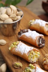 Delicious cannoli with ricotta cheese, peanuts, pistachios, chocolate and powdered sugar on table, closeup