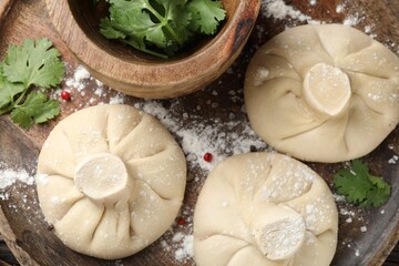 Uncooked khinkalis (dumplings) with peppercorns and parsley on wooden table, top view