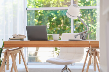 Home workspace. Laptop and stationery on wooden desk near window indoors