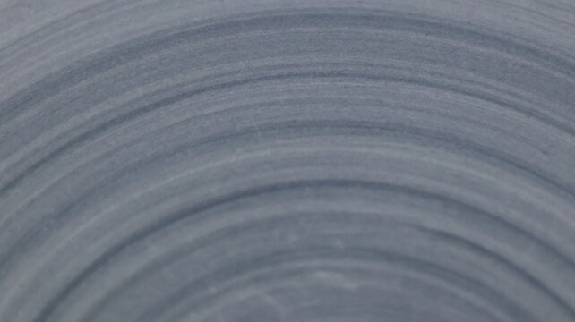 Concentric ripple rings etched on smooth gray blue surface background, abstract circular texture with soft radial rhythm and polished tonal depth