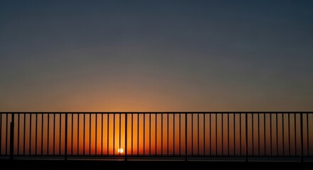 Obraz premium Sunset behind railing with warm sky gradient creating peaceful evening silhouette view.