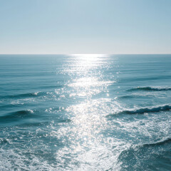 Fototapeta premium Sunlight sparkles on calm ocean waves under a clear blue sky, creating a serene and peaceful seascape with gentle ripples and shimmering reflections