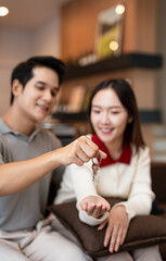 Happy young family couple holding key to new home on moving day concept, first time real estate owners man husband embrace woman wife look at camera proud buying property sitting in own flat .