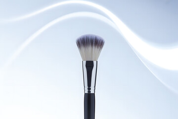 Close-up of a professional makeup brush with soft brown and pink bristles on a white background