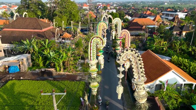 Real time aerial view of drone forward flight of rows of Penjor decorations on the road in Bali with bright colors