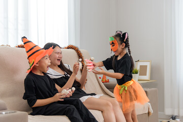 Family members in costumes are celebrating halloween day, a child in a pumpkin mask offers a doll...
