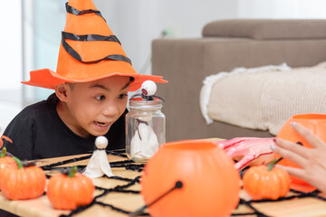 Young boy wearing a witch hat looks intently at a spooky jar with a spider, halloween pumpkins and...