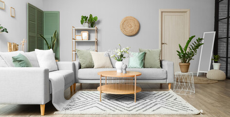 Interior of modern living room with grey sofas, flower vase on coffee table and houseplants