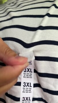 Vertical 4K video. Fat adult man in white T-shirt with stripes removes 3XL sticker. Concept of buying new clothes of Extra Large size, Black Friday sale, shopping in mall, fitting, weight loss. Shop