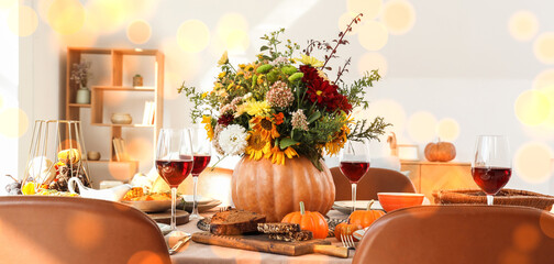 Pumpkin with autumn bouquet on festive dining table in room, closeup
