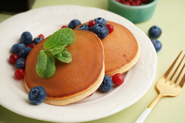 Tasty pancakes with berries on green background