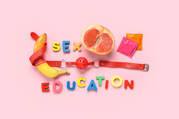 Text SEX EDUCATION with condoms, fresh fruits and mouth gag on pink background
