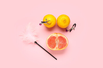 Fresh citruses with feather stick and nipple clamps on pink background. Sex education