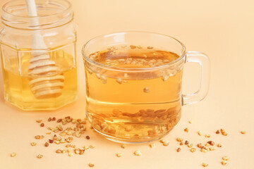 Glass cup of fresh tasty buckwheat tea and honey on beige background, closeup