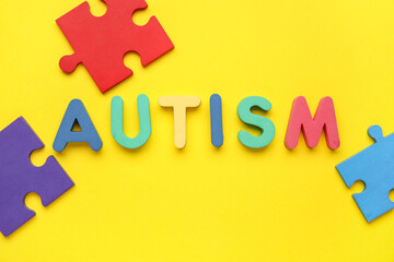 Word AUTISM and colorful puzzle pieces on yellow background. Top view