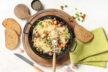 Frying pan with tasty pasta, mushrooms and bread on light background