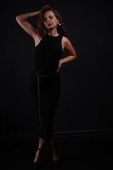 Fototapeta premium Low key portrait of pretty brunette woman in black dress full length