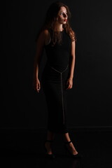 Fototapeta premium Low key portrait of pretty brunette woman in black dress full length