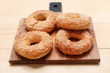 Cutting board of tasty bagels with sesame seeds on wooden background, closeup