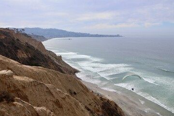 Coastal cliff view with a paraglider soaring above the ocean near a beach at sunset in San Diego, California