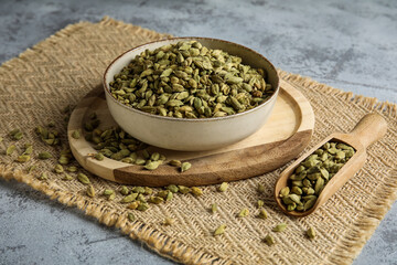 Bowl and wooden scoop with cardamom spice on grey background