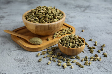 Wooden bowls of cardamom spice and spoon with powder on grey background
