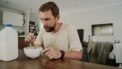 Caucasian man, 35 years old, enjoys a bowl of cereal with milk in a serene kitchen. Calm atmosphere enhances the peaceful moment.