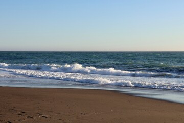 Calm ocean waves gently lapping on a sandy beach during a clear afternoon along the coastline