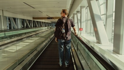 Middle-aged man stands calmly on moving walkway in airport terminal. Peaceful atmosphere enhances contemplative mood during daytime.
