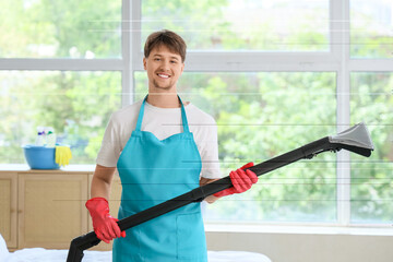 Young male janitor with modern vacuum cleaner in bedroom