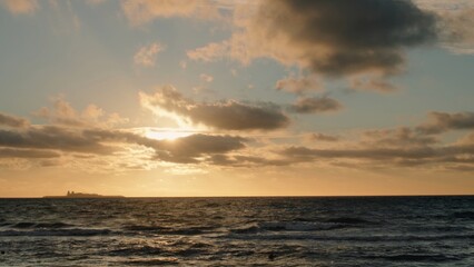 Serene ocean sunset paints sky with vibrant hues. Tranquil scene features gentle waves lapping at seashore, distant land visible.