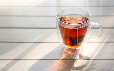 Glass cup of black tea on white wooden table