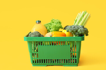 Green shopping basket with different fresh products on yellow background