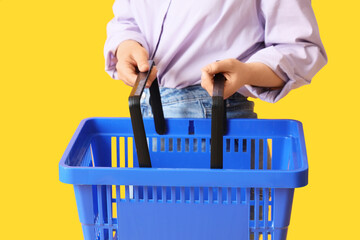 Fototapeta premium Woman with blue shopping basket on yellow background