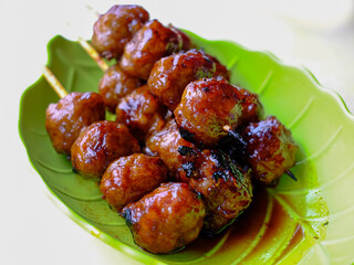 Mouthwatering Indonesian street food: grilled meatballs (Bakso Bakar) glistening with sauce, ready to eat