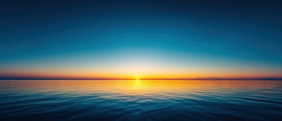 Obraz premium Stunning ocean sunset with vibrant orange and yellow hues over calm water and clear blue sky creating a tranquil natural scene